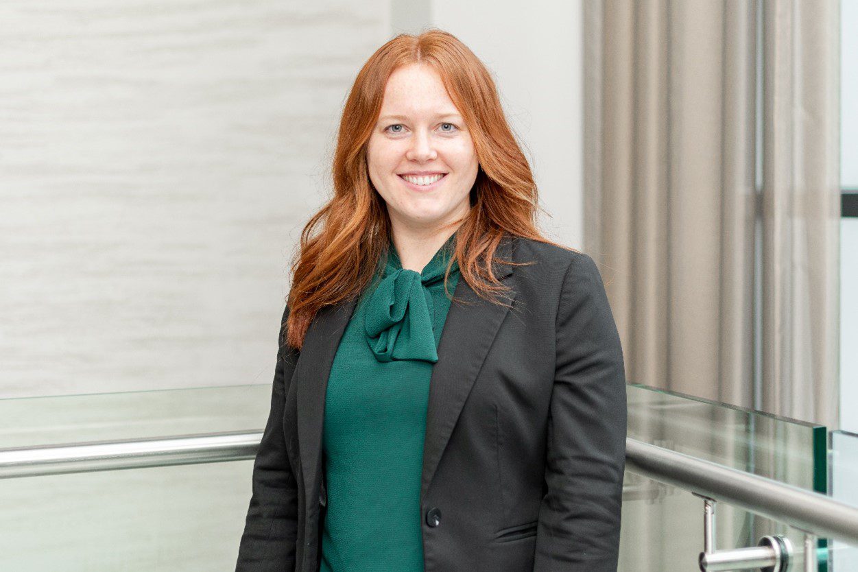 Kirstie Orton head shot image, wearing a green blouse and dark grey suit jacket, with auburn hair.