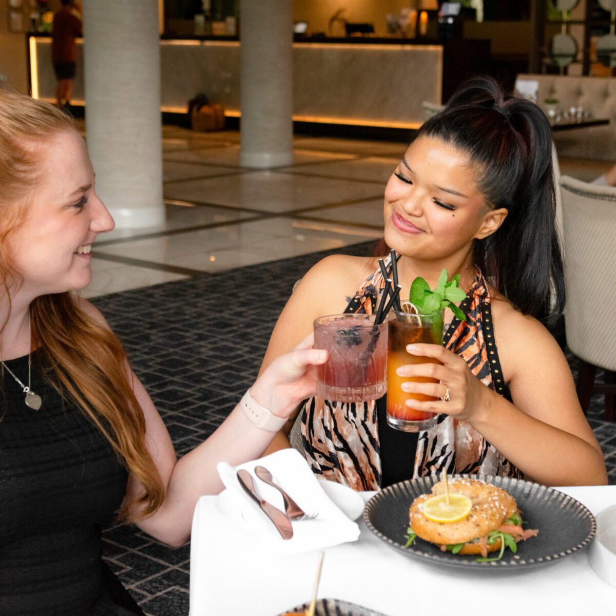 two girls looking a each other and smiling whilst holding cocktais