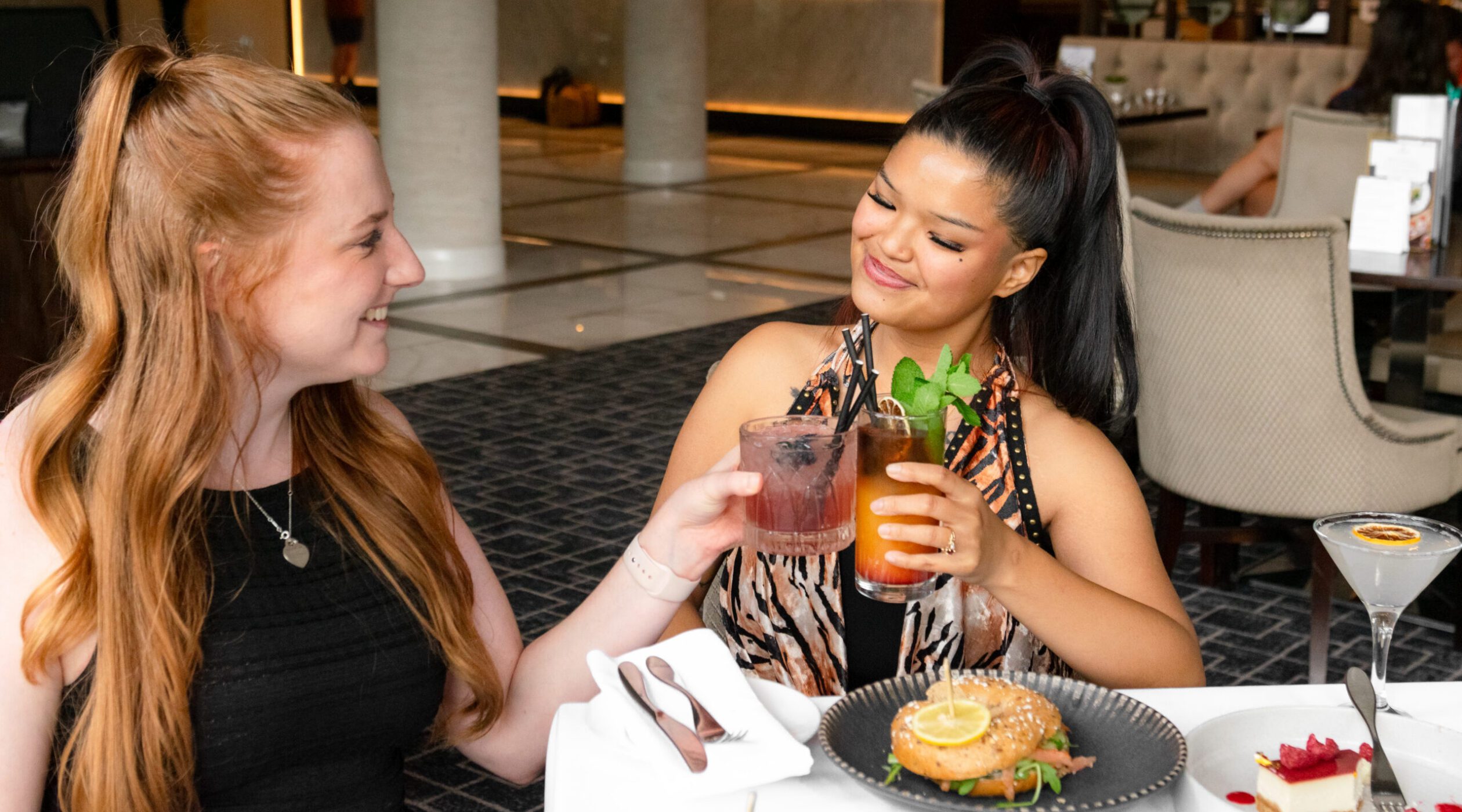 . bottomless brunch in Birmingham. Two girls looking a each other and smiling whilst holding cocktais