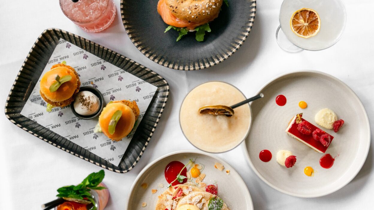 selection of dishes as part of Park Regis Birmingham's Bottomless Brunch menu. Features mini chicken burger sliders, cheesecake, smoked salmon a seeded bagel, and pancakes.